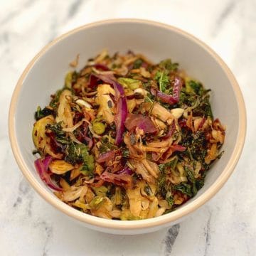 Trader Joe's Cruciferous Crunch (a mixture of thinly sliced purple cabbage, kale and Brussels sprouts), braised with garlic, olive oil and vinegar in a white bowl on a gray marble background.