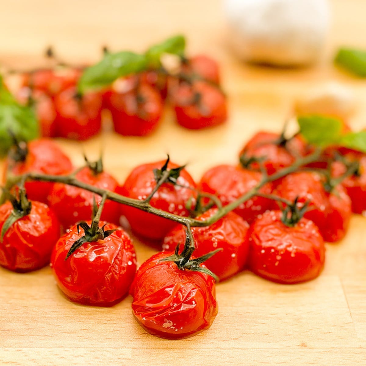 Roasted cherry tomatoes on the vine with basil and garlic on a butcher block cutting board