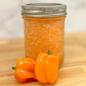 Pineapple habanero sauce in a glass jar with two habaneros on a butcher block counter.