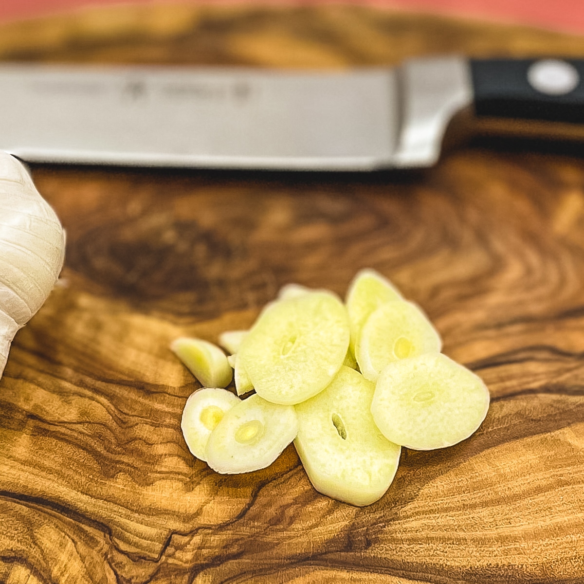 Sliced garlic on a wooden cutting board.