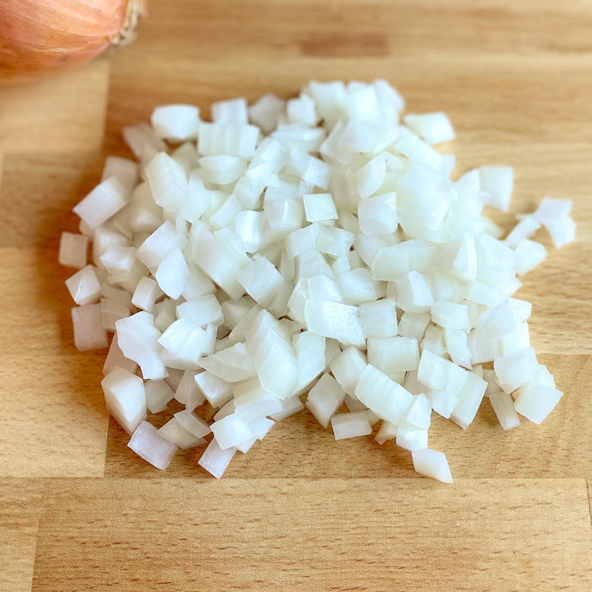 Diced yellow onion with a yellow onion in the background on a butcher block cutting board