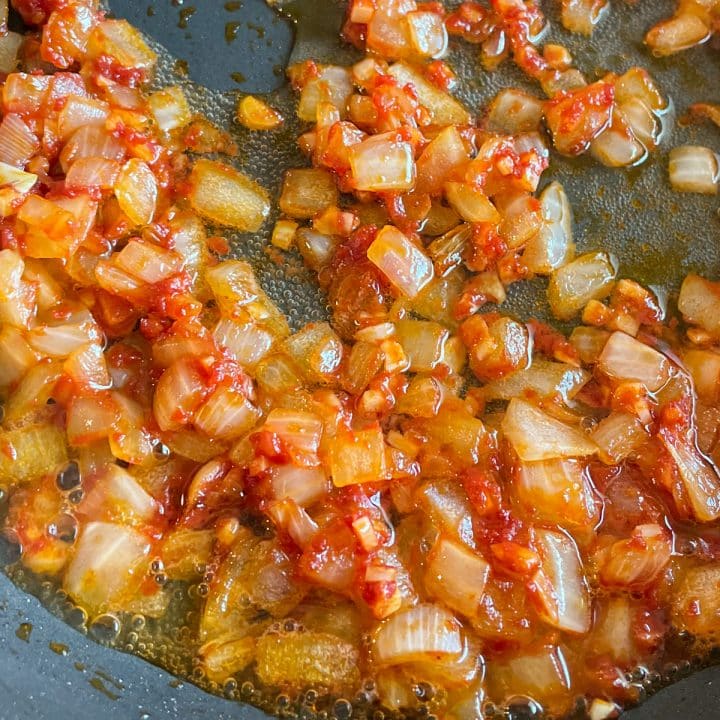 Sautéed onion, garlic, tomato paste, and white wine in a black frying pan