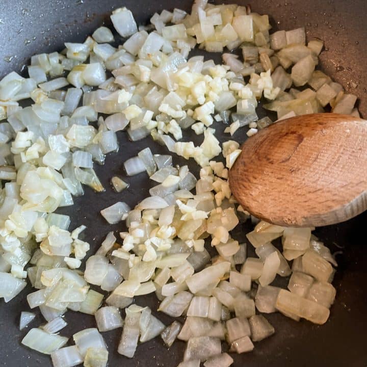 Sautéed onions and garlic in a black frying pan with a wooden spoon