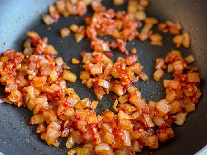 Sautéed onion, garlic, and tomato paste in a black frying pan