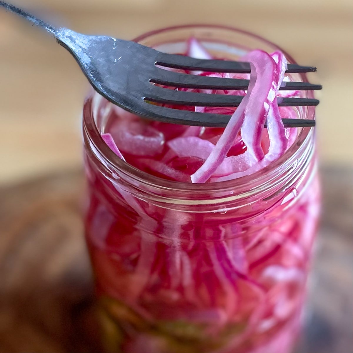Sliced red spicy pickled onions are lifted out of a glass Mason jar with a silver fork.