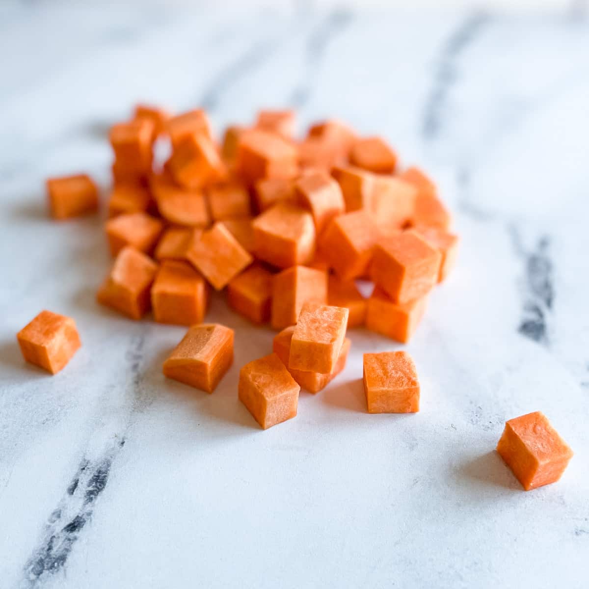 A pile of sweet potato cubes sits on a white marble counter top.