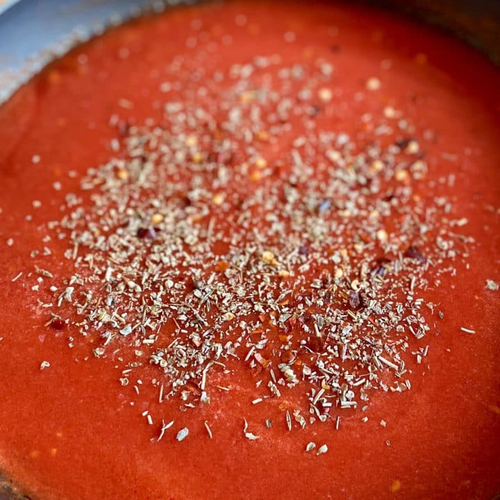 Tomato sauce in a black frying pan sprinkled with salt, chili flake, and Italian seasoning