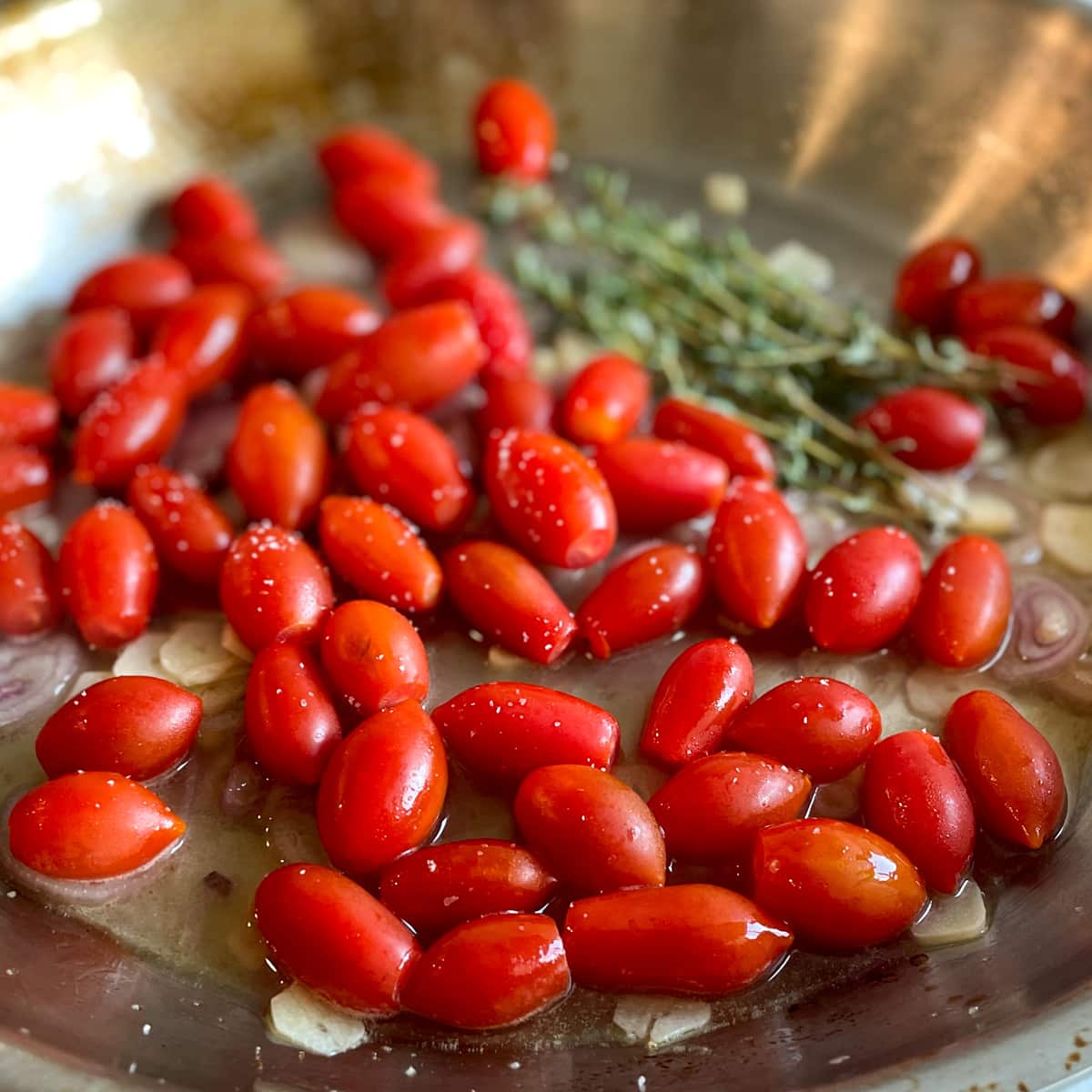 Fresh cherry tomatoes and thyme sit in a stainless steel pan with sliced garlic, sliced shallots, lemon juice, white wine, and salt.