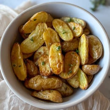 Air Fryer roasted fingerling potatoes dressed in olive oil, lemon juice, garlic, and thyme dressing with a white linen and thyme and lemon in the background.