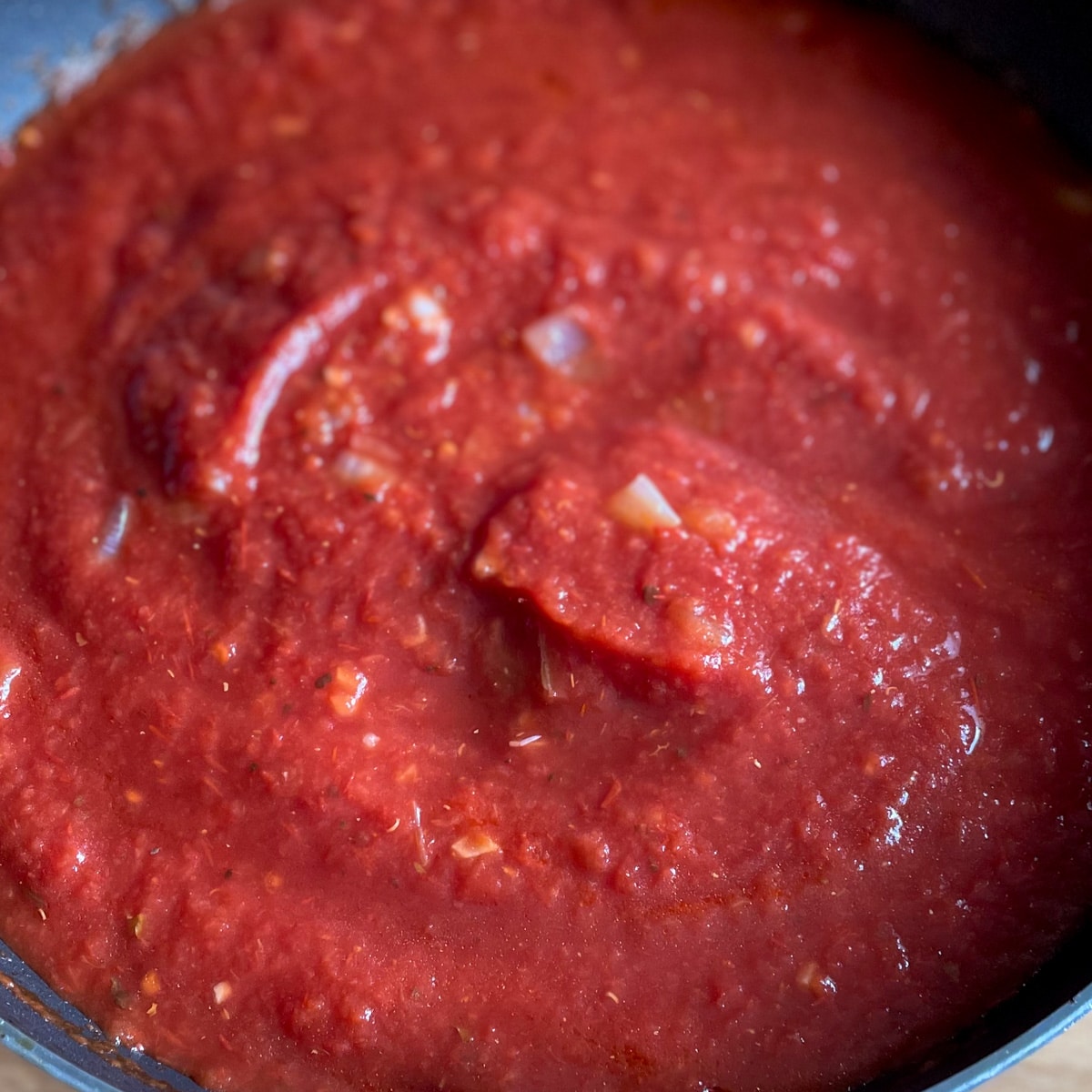 Closeup shot of arrabbiata sauce with tomatoes added to pan with onions, garlic, and Calabrian chilis