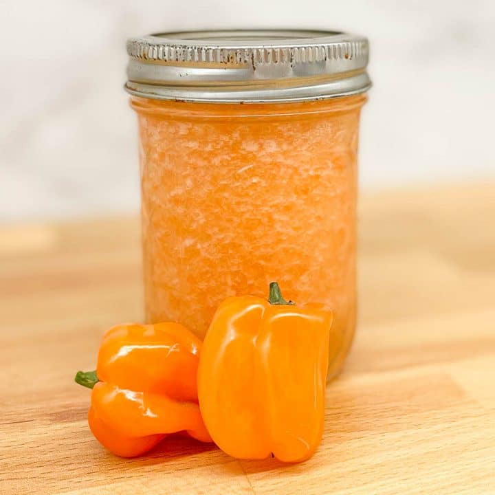 Pineapple habanero sauce in a glass jar with two habaneros on a butcher block counter.