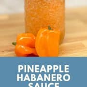 Pineapple habanero sauce is shown in a glass jar on a wooden cutting board with two habanero peppers in the foreground.