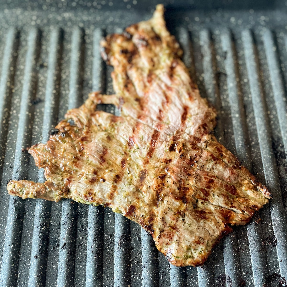 Ranchera meat with grill marks is shown cooking on a grill pan.