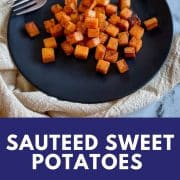 Sauteed sweet potatoes sit on a black dish with a fork and a cream-colored linen on a white marble counter.