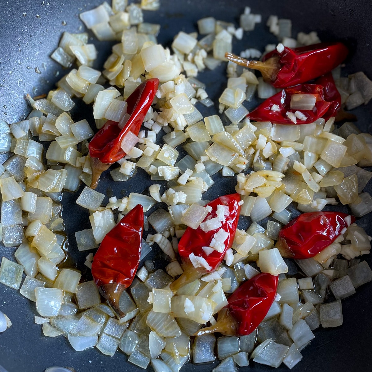 Sweating diced onion, whole Calabrian chilis, and minced garlic are pictured in a black pan.