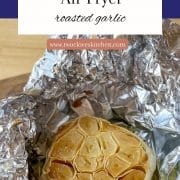 Roasted Garlic is shown in tin foil on a wooden cutting board with the title of the recipe and the URL for Two Cloves Kitchen.