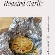 Roasted Garlic is shown in tin foil on a wooden cutting board with the title of the recipe and the URL for Two Cloves Kitchen.