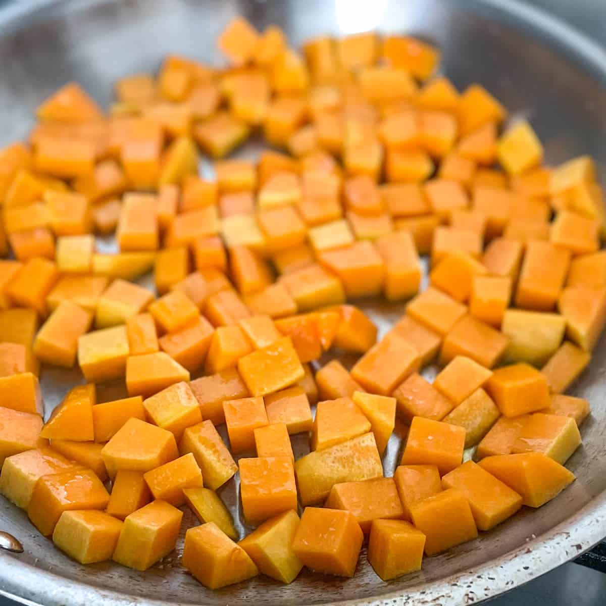 Cubed butternut squash is shown in a pan with olive oil.
