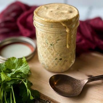 Chipotle sauce in a glass jar sits on a wooden cutting board with a spoon, parsley and a red linen.