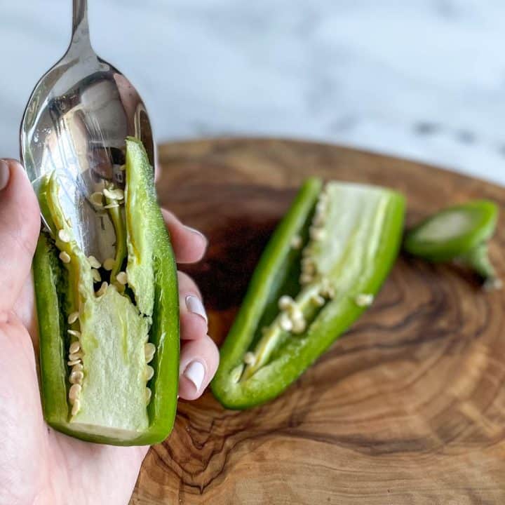 A silver spoon scoops out the membrane and seeds from a jalapeno.