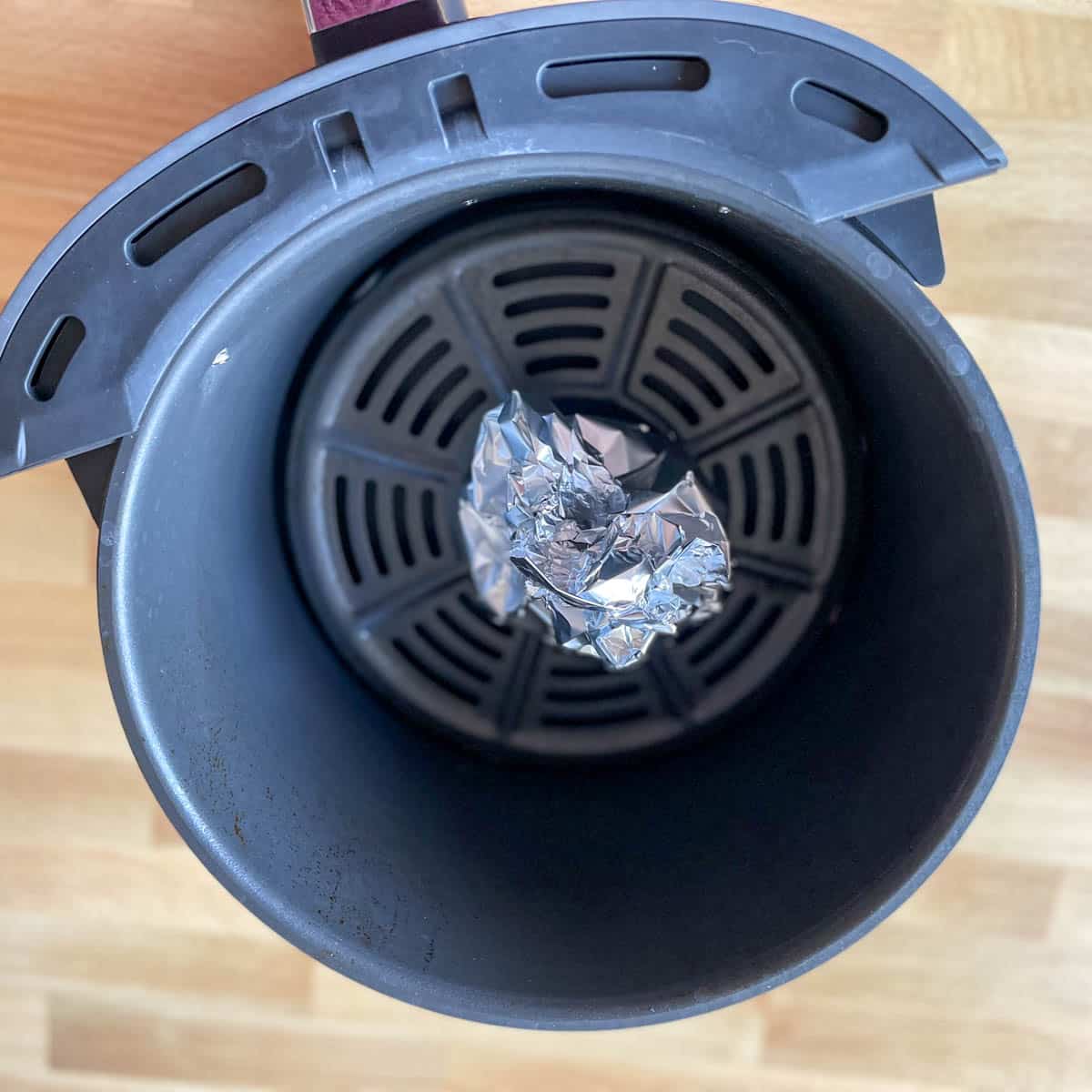 A ball of foil containing a cut head of garlic is shown in the basket of an air fryer.