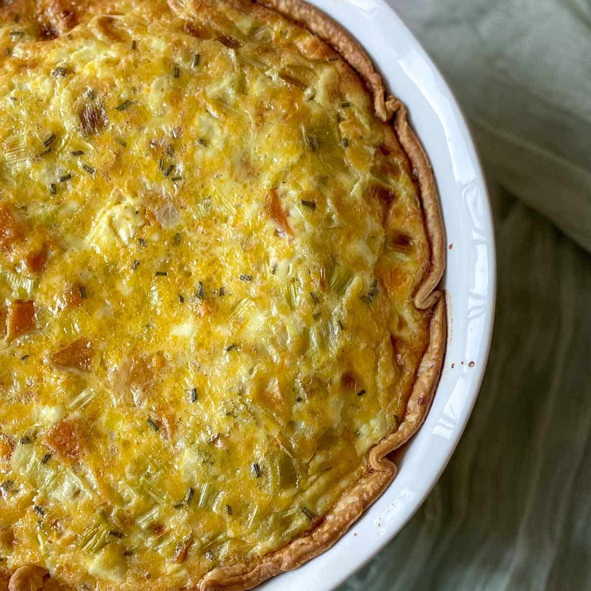 A closeup of the finished quiche is shown in a white pie plate with a light green linen in the background.