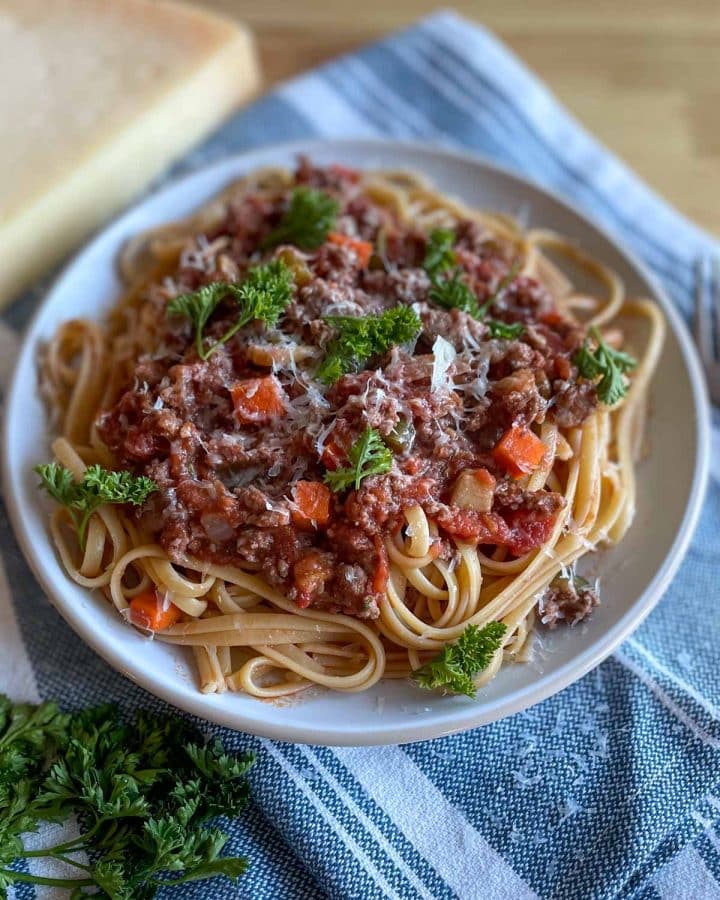 A plate of linguine bolognese is topped with parmesan cheese and parsley.