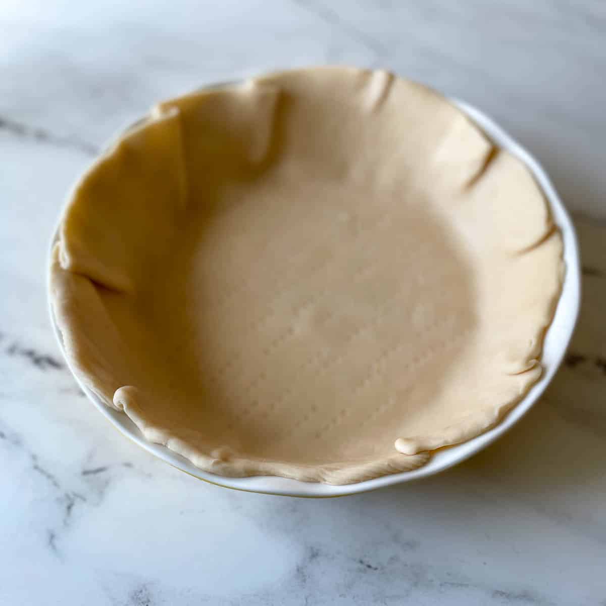 a pie crust with fork many fork indentations is shown in a white pie plate.
