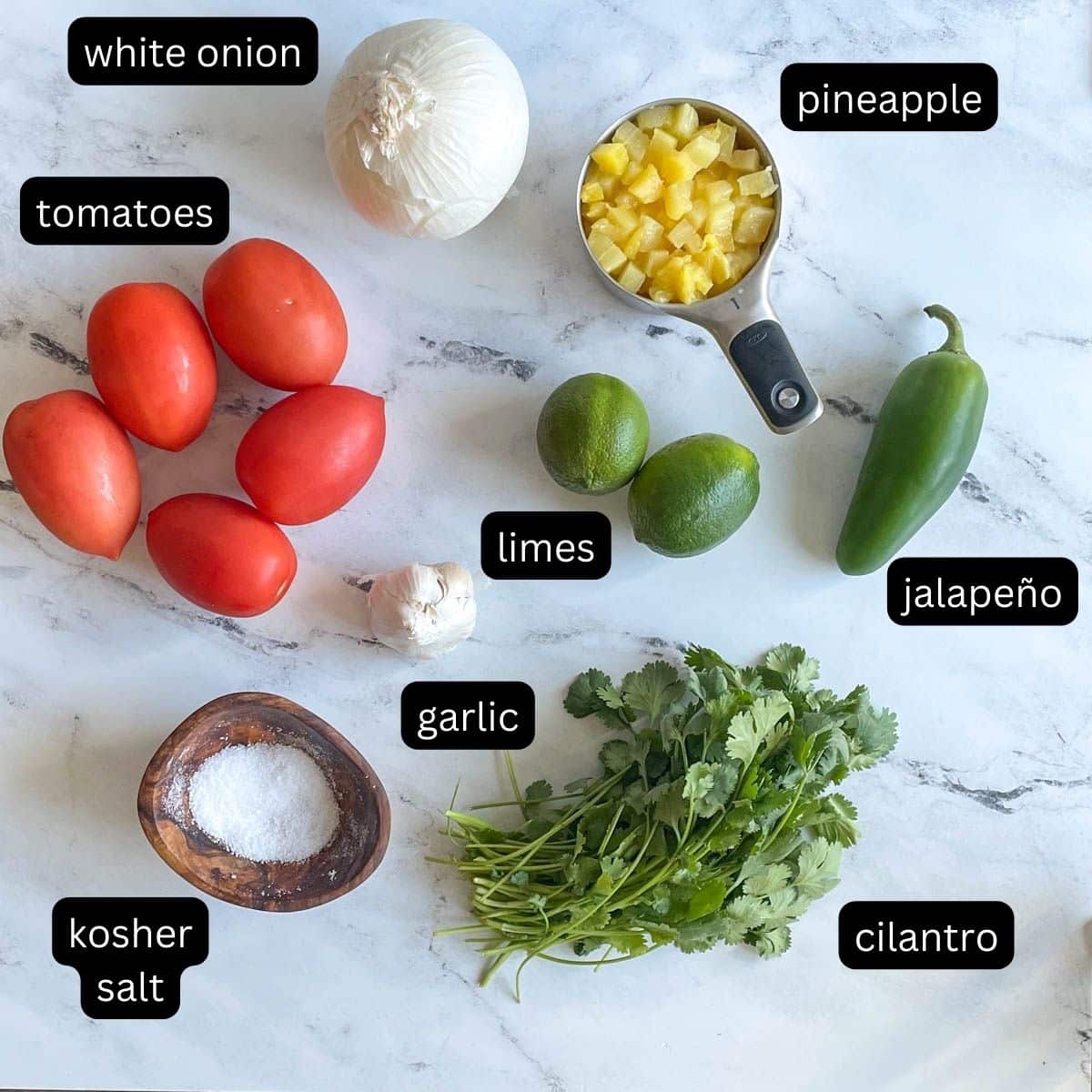 Labeled ingredients for pineapple pico de gallo sit on a white marble counter.