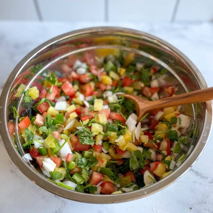 Finished pineapple pico de gallo is shown in a stainless steel bowl with a wooden spoon.
