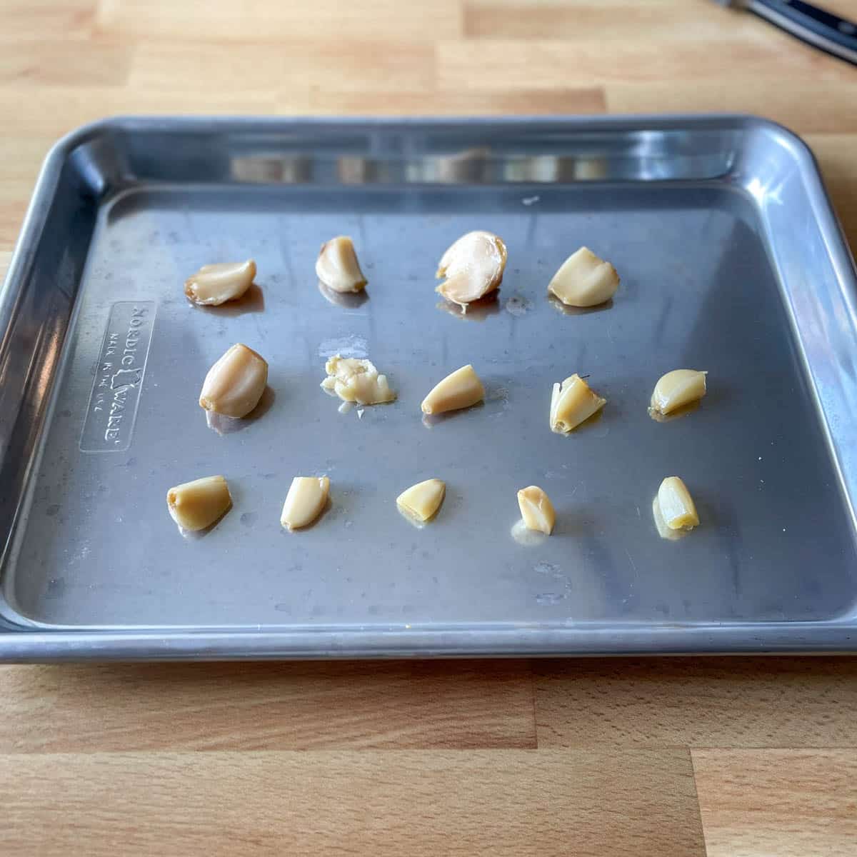 Peeled single cloves of garlic are shown in three lines on a small baking sheet.