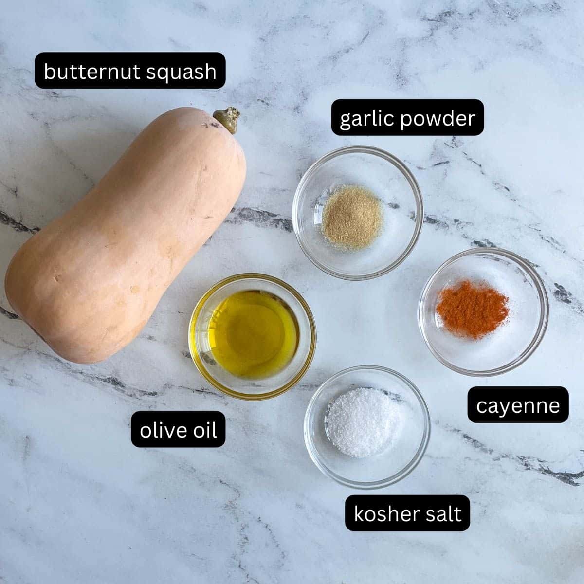 Labeled ingredients sit on a white counter: a butternut squash, olive oil, kosher salt, garlic powder, and cayenne.