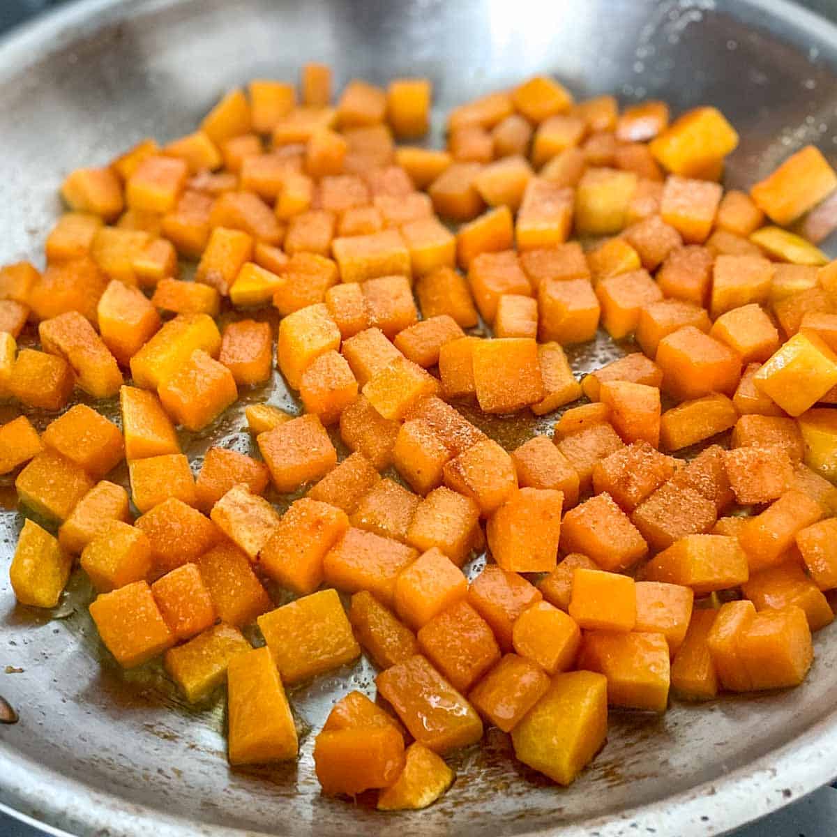 Cubed butternut squash is shown sautéeing in a pan sprinkled with salt, garlic powder, and cayenne.