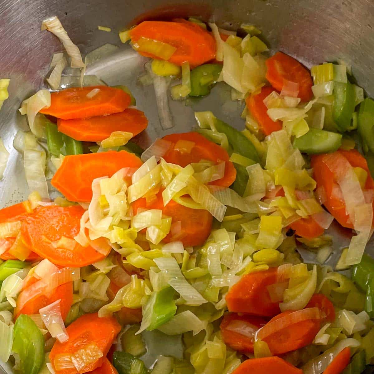 Sauteed carrot, celery, and leek are shown in a stainless steel pot.