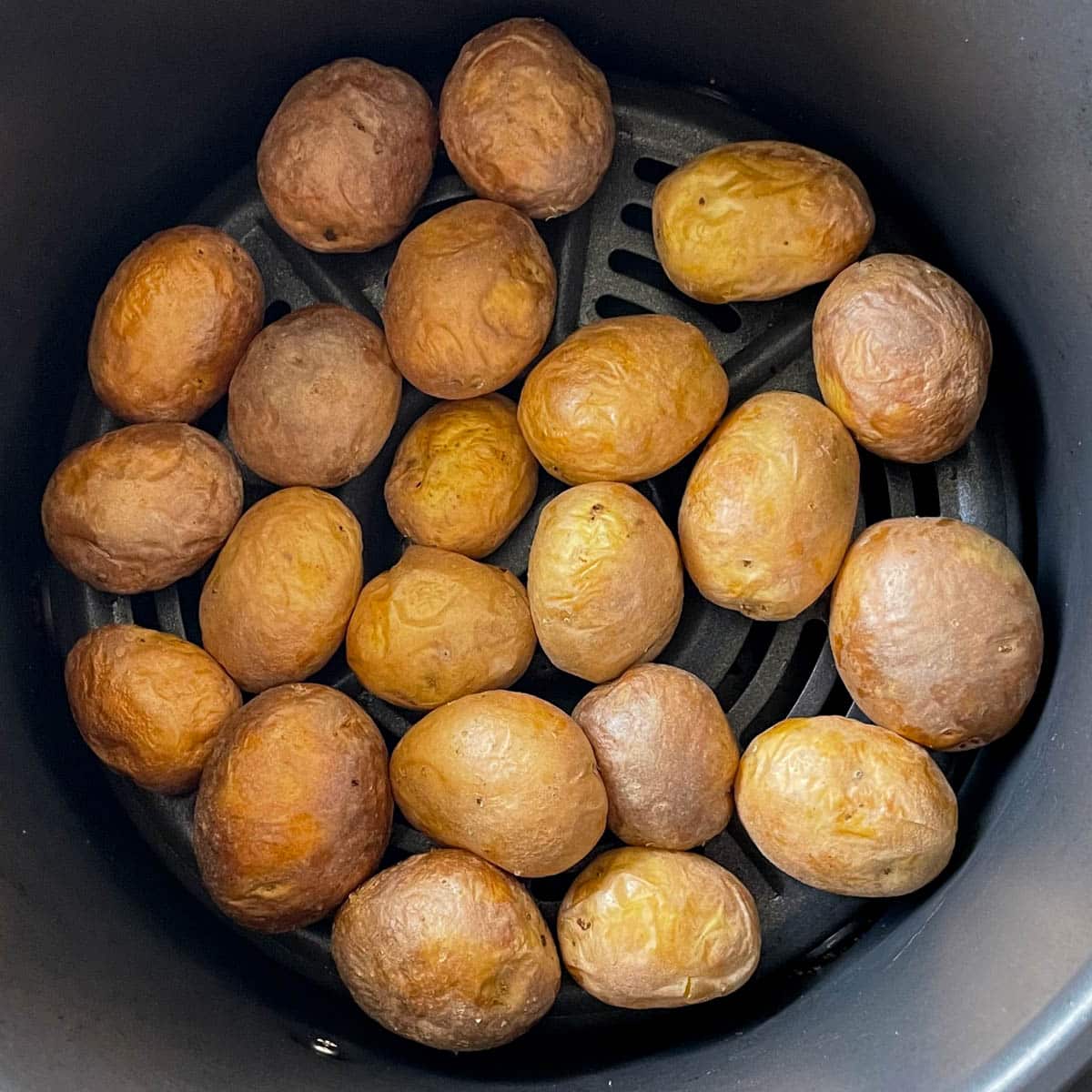 Roasted baby yellow potatoes are shown in the base of an air fryer basket.