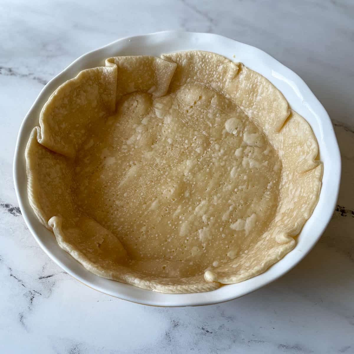 A blind baked pie crust sits on a white marble counter.