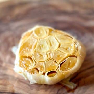 Roasted garlic is shown on a wooden cutting board.