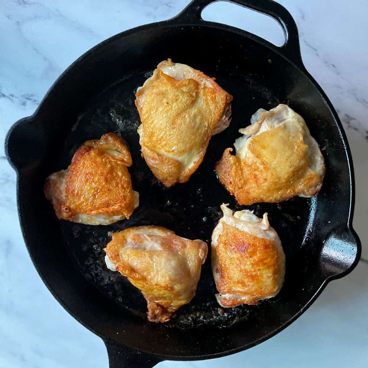 Five golden brown chicken thighs sit in a black cast iron pan.