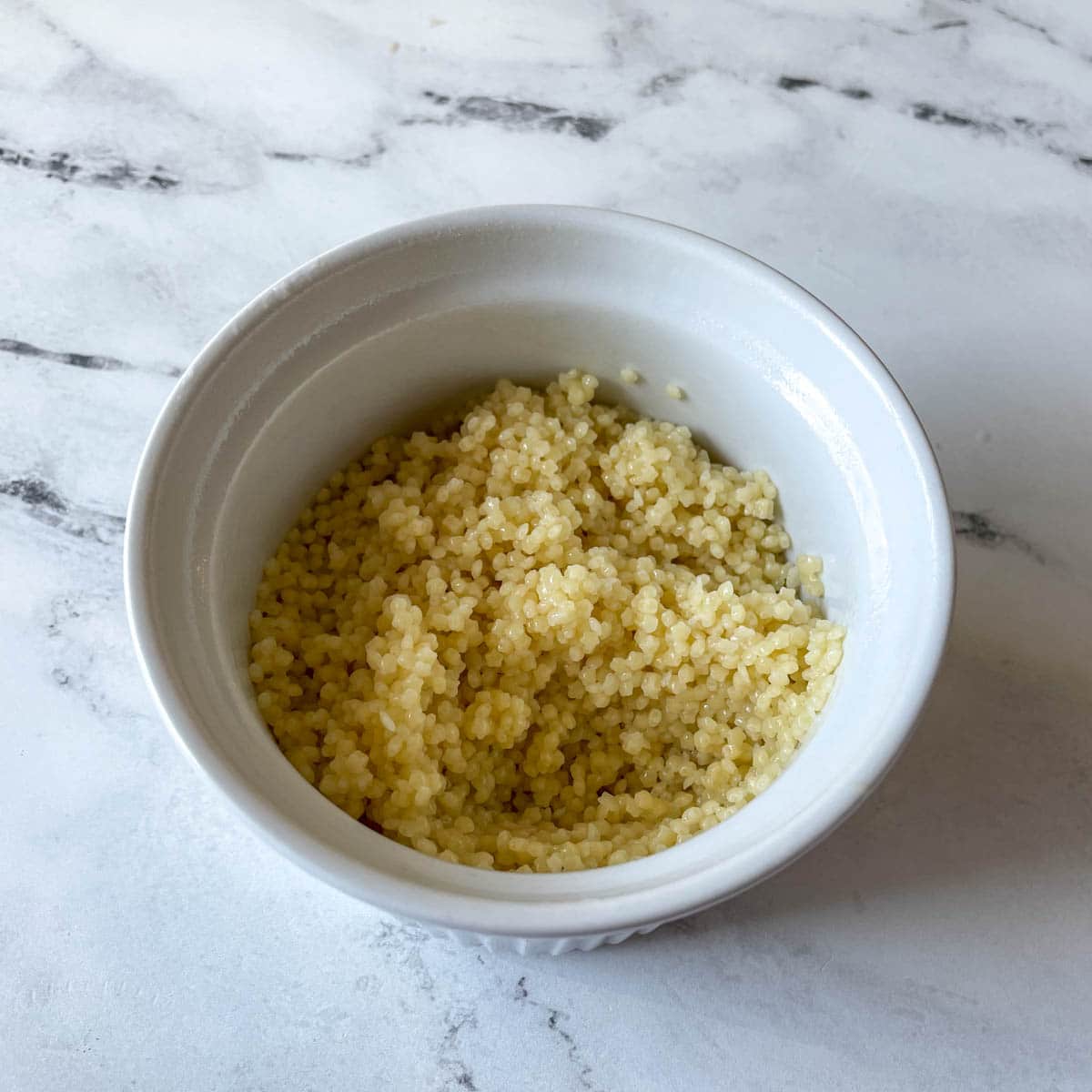 Cooked pastina coated in olive oil is shown in a white ramekin.