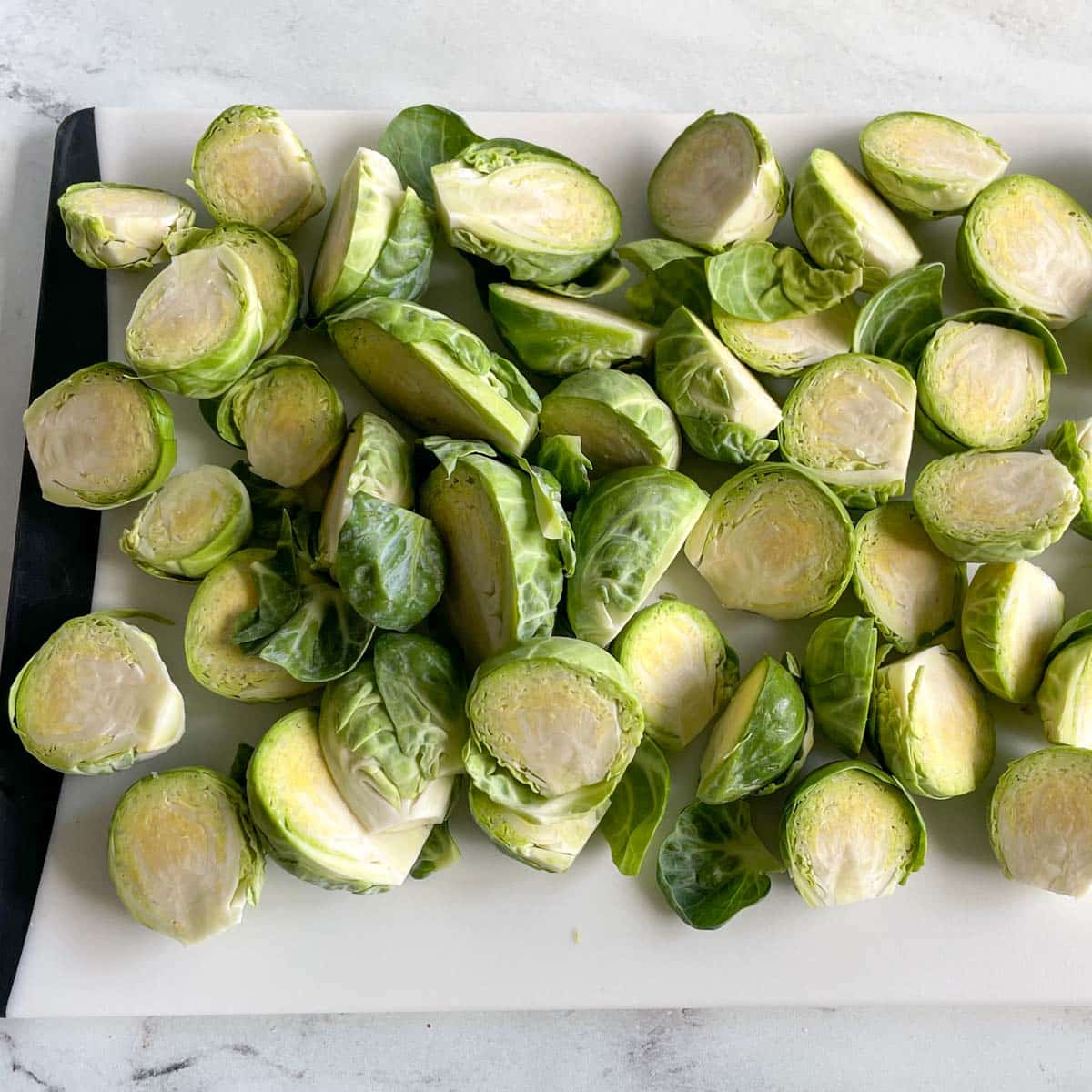A cutting board is covered in halved Brussels sprouts.