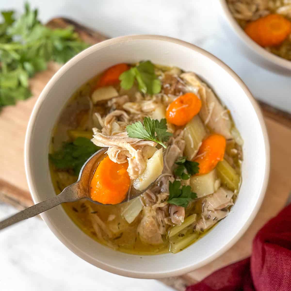 A white bowl of Instant Pot Chicken Stew sits on a rustic wooden cutting board with a red linen on a white marble counter.