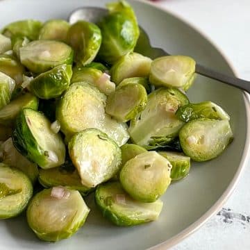 Marinated brussels sprouts are shown on a white plate with a spoon and a dark red linen in the background.