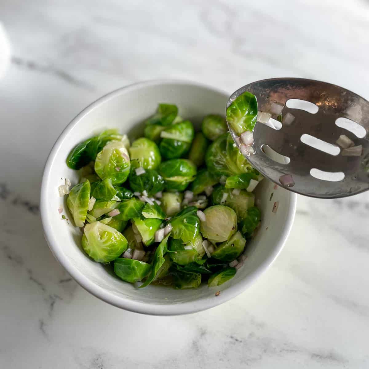 Halved brussels sprouts and marinade are mixed together with a slotted spoon.