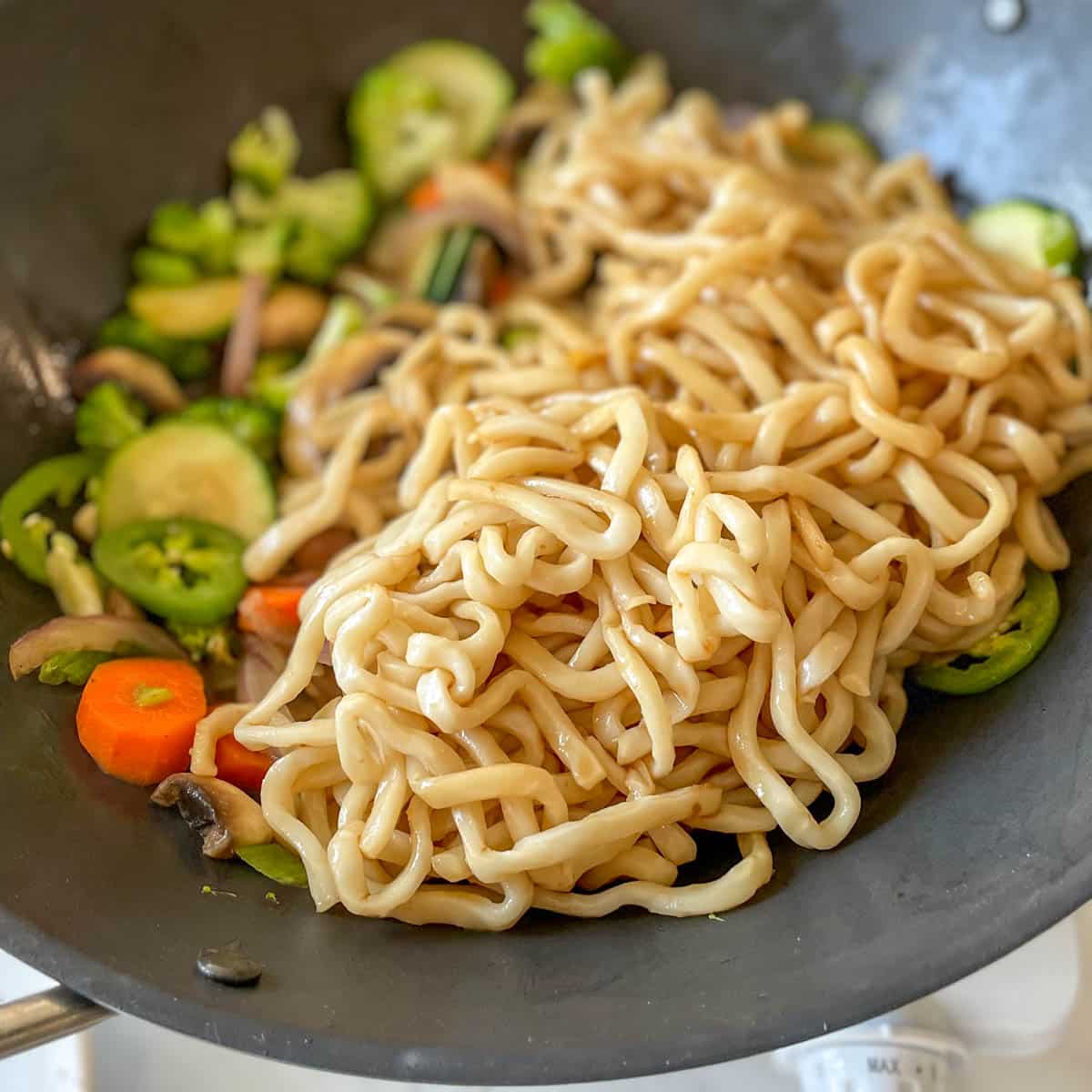 Noodles are added to the wok with vegetables.