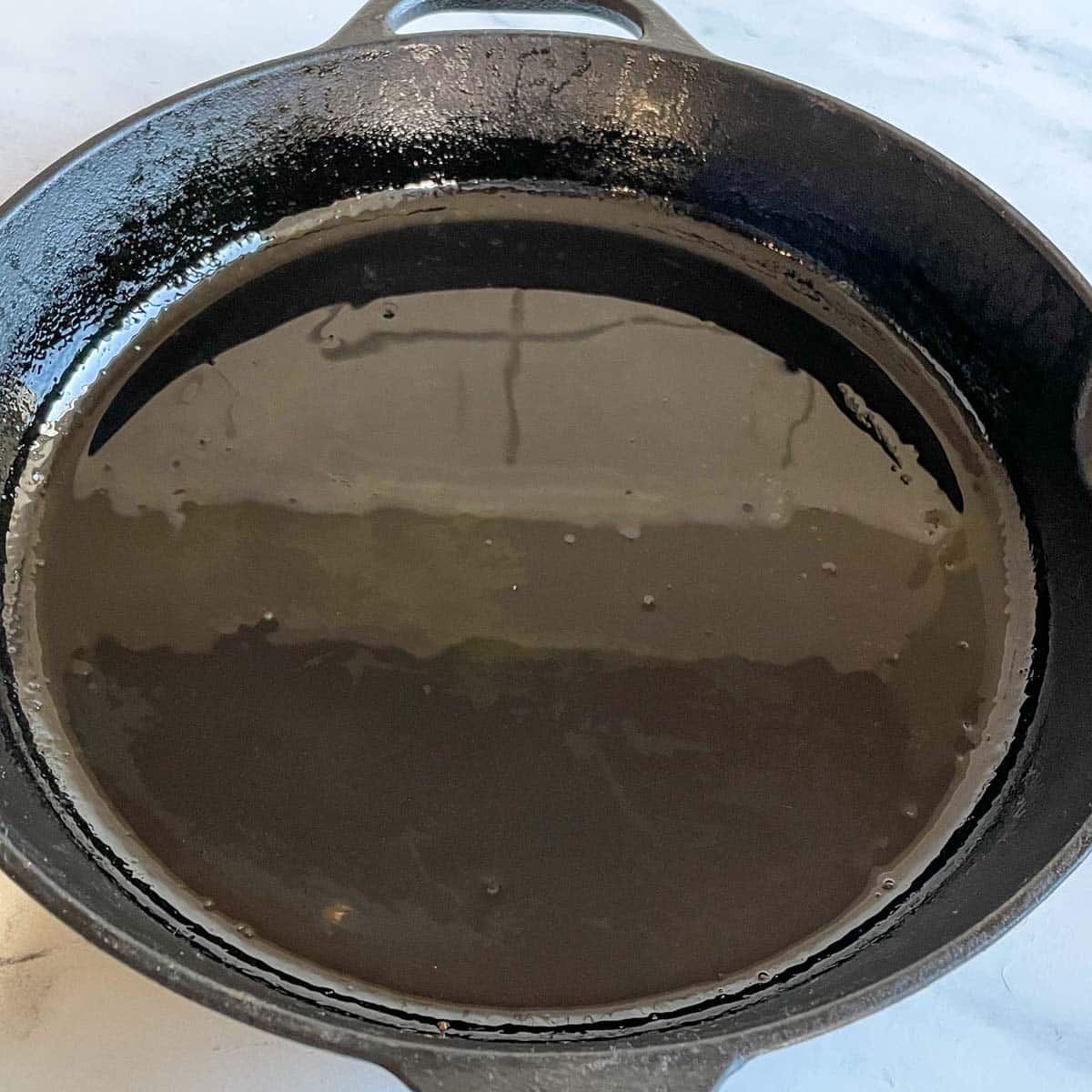 A cast iron pan is shown with a layer of grapeseed oil in the bottom.