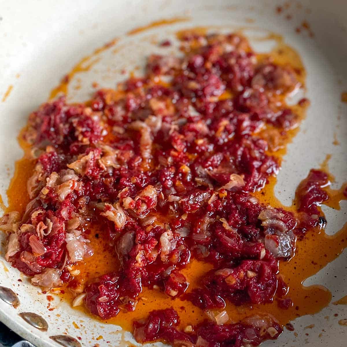 Tomato paste is added to the garlic, shallot, olive oil, and pancetta mixture.