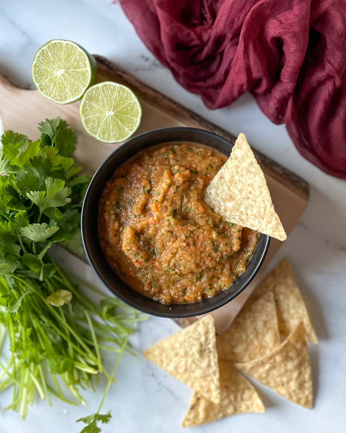 A bowl of pineapple habanero salsa sits on a rustic wooden cutting board surrounded by limes, cilantro, and tortilla chips.