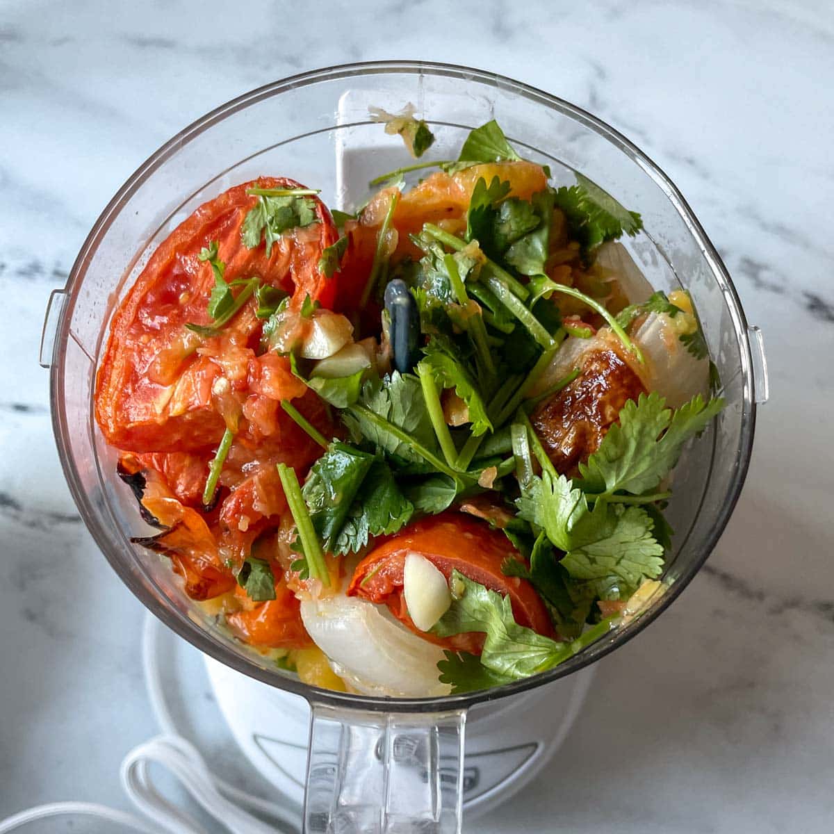 The roasted ingredients for pineapple habanero salsa are shown in a mini food processor.