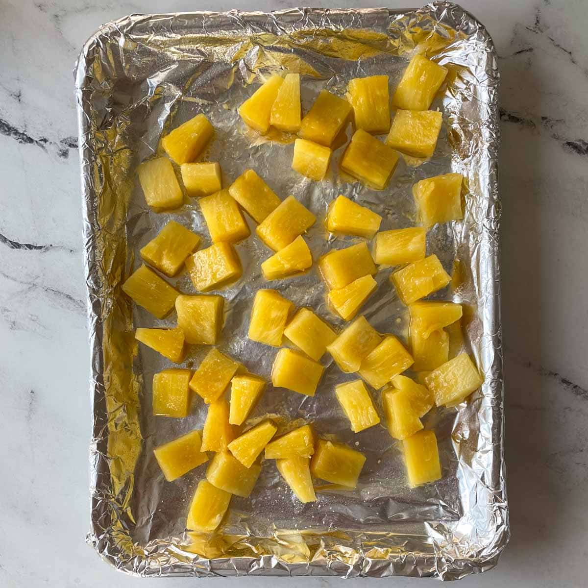 Pieces of pineapple sit on a sheet tray.