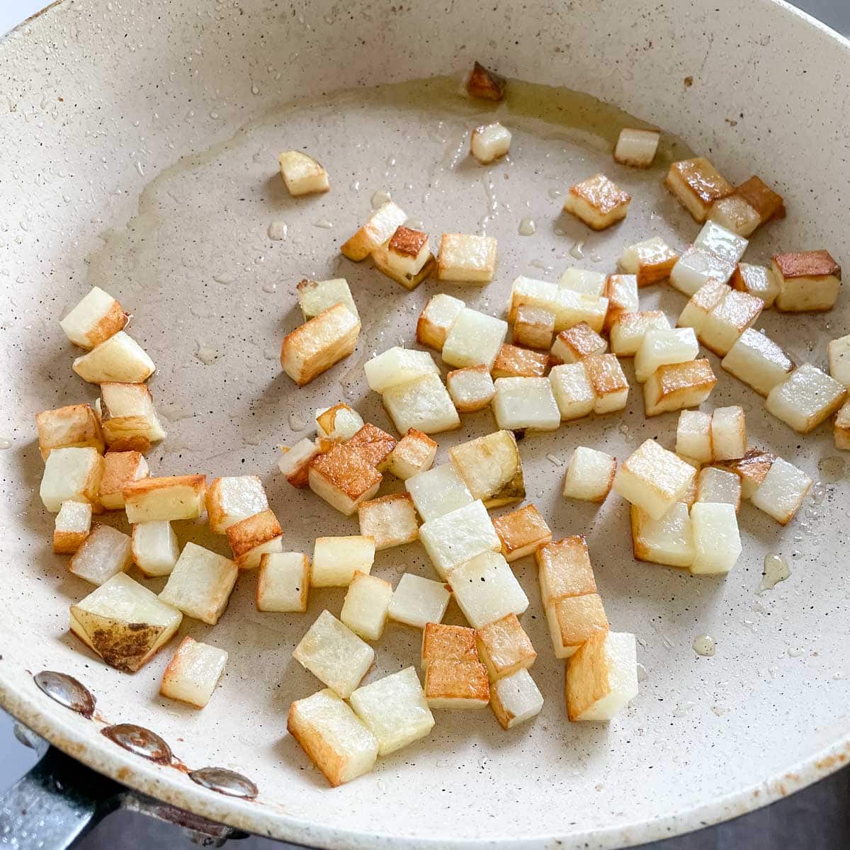 Browned potatoes are shown in a white pan.